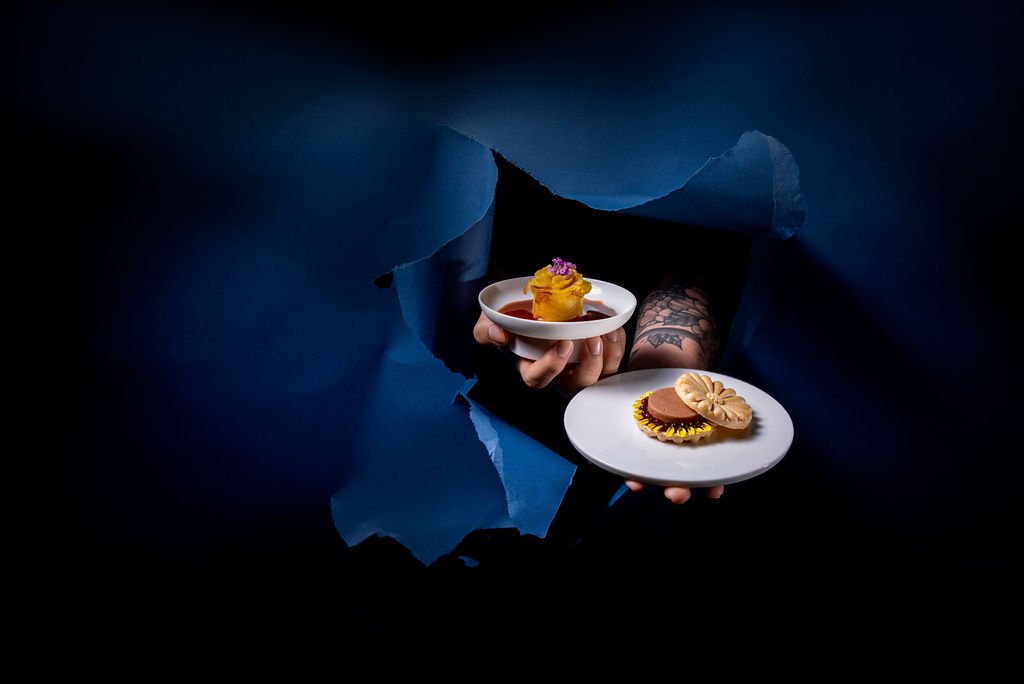Two small plates with canapés held through torn dark-blue paper.