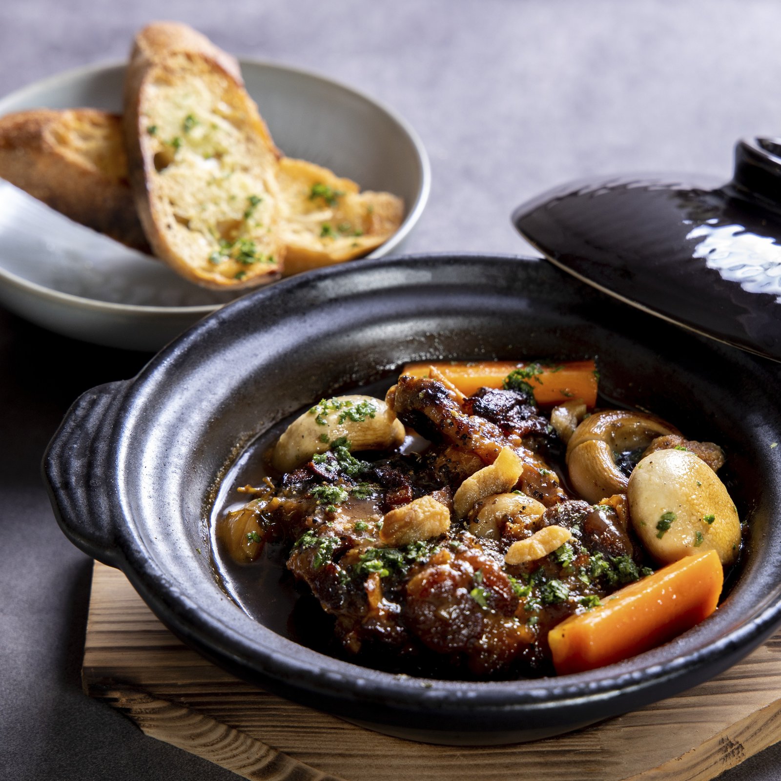 Coq au vin at Bouchon Enfin — chicken braised in red wine in a black donabe with carrot, button mushroom, and garlic toast in a side bowl.