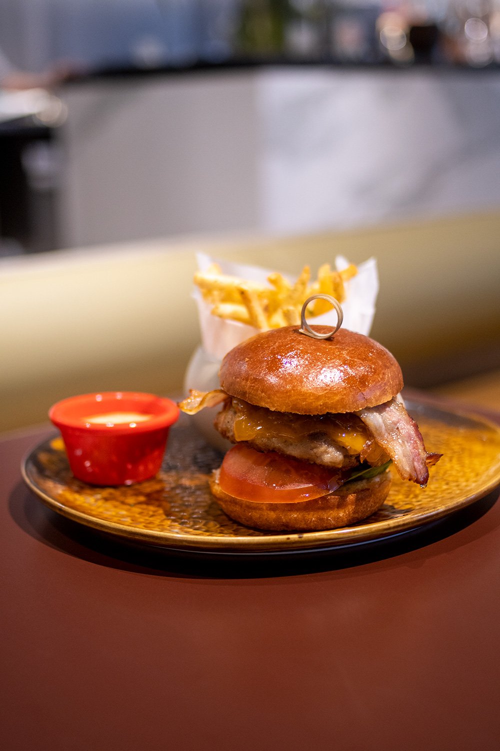 Bouchon Enfin pork burger — brioche bun, melted cheese, smoked bacon, tomato, with shoestring fries in a paper cone.