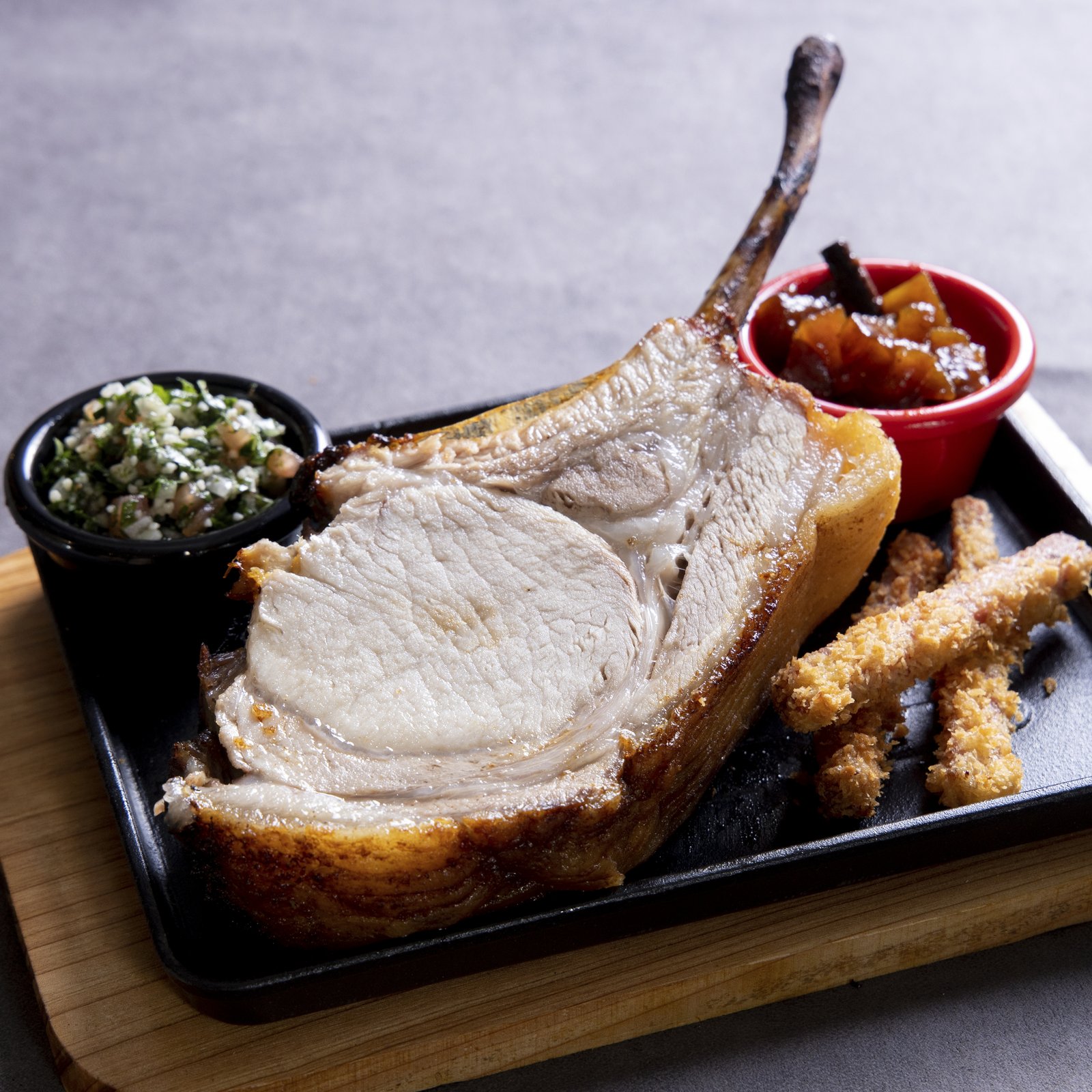 Bouchon Enfin pork chop on the bone — house-aged, served with chimichurri tabbouleh, fried pork puffs, and fruit chutney.